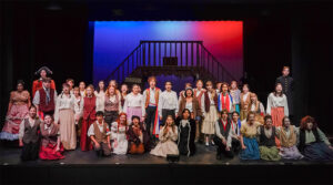Photo of the cast of Les Misérables School Edition singing out to the audience. The whole cast is spread across the stage, singing together at the end of the show.