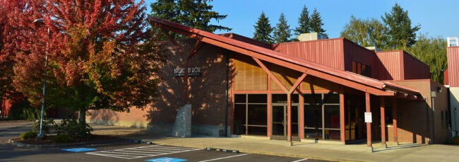 Photo of the Broadway Rose New Stage theater entrance in the fall at sunset. Brilliant reds and oranges color this photo, both in the trees and in the amber light of the sunset on the building.