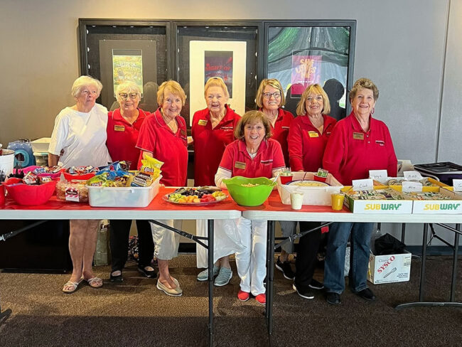 Photo of the guild providing lunch for the crew and interns who are loading in all of the summer shows at the Deb Fennell Auditorium. There are eight guild members here, all smiling for the camera as they get the food and tables set up.