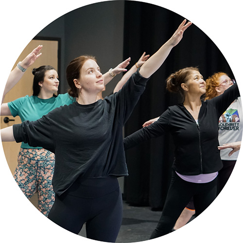 A photo of multiple people all posing dramatically with their arms outstretched in one of our adult jazz dance classes.