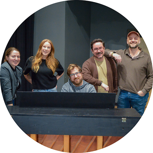 Photo of several performers all gathered around a piano and smiling for the camera.