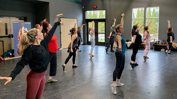 Jazz - Intermediate Advanced 02 Photo from one of our Adult Dance classes showing the students mid dance number, posing with their left arms raised above their heads and their right arms out to the side.