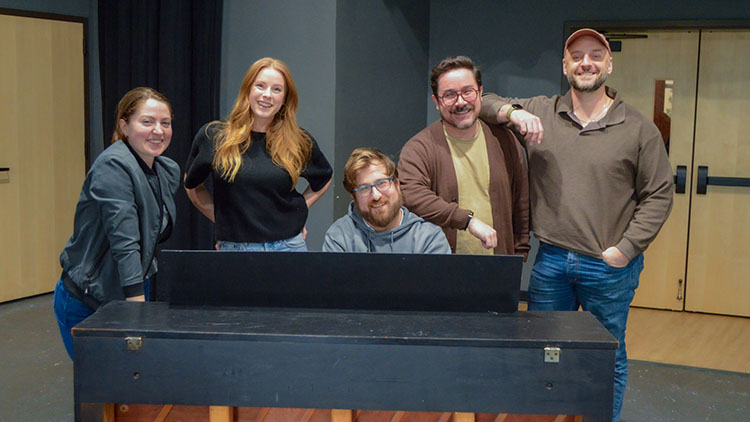 Musical Theatre Audition Workshop Photo of several performers all gathered around a piano and smiling for the camera.