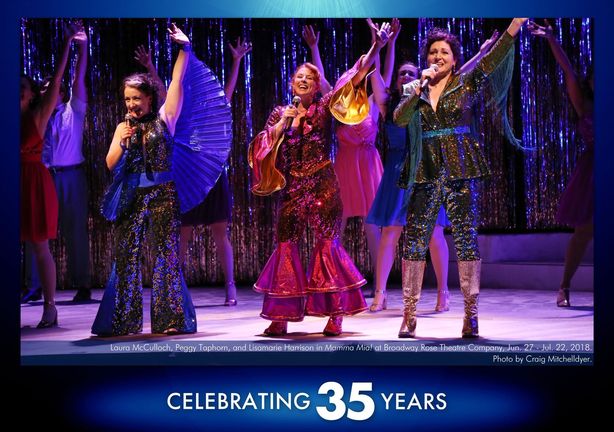 Mamma Mia A photo from Mamma Mia showing three women in sparkling blue, pink, and green outfits doing disco moves while they sing out to the audience holding handheld microphones.