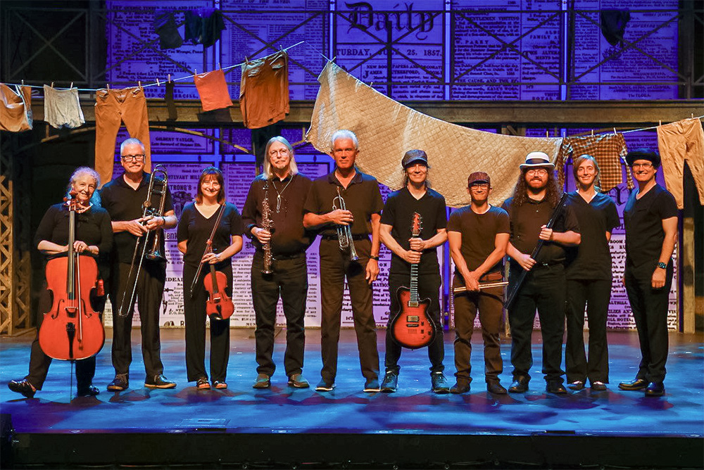 Photo of the Newsies band standing across the front of the stage holding their instruments. Names listed with their instruments in this section.