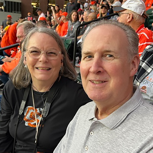 A photo of Joann and Gerry Reese at an Oregon State University football game, sitting in the stands, smiling to the camera.